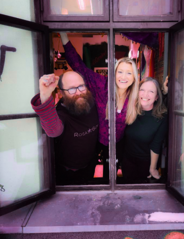 Three people looking out of an open window - pink tones colour with letters on the side